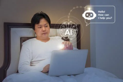 A man sits on a bed using a laptop with glowing AI assistant interface, com.. Stock Photos