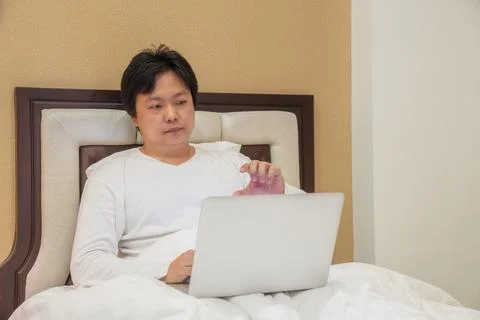 Man sits on bed using laptop while raising hand toward screen, combining re.. Stock Photos