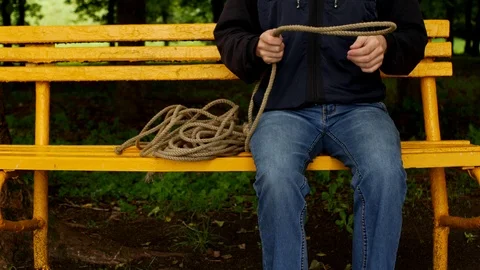 A man sits on a bench and makes a loop from the rope, prepares for suicide 스톡 동영상 95100502