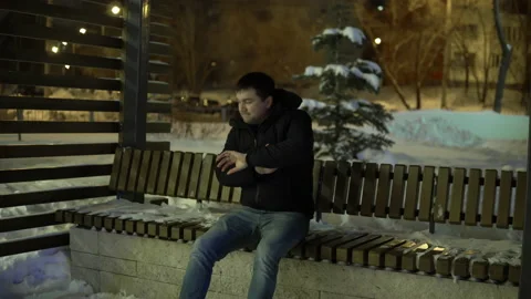 A man sits on a bench in the evening winter time and is not impatiently waiting Stock Footage 146811703