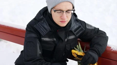 Man sits on bench at snowy winter day and shows bag with fruits Stock Footage 276361636