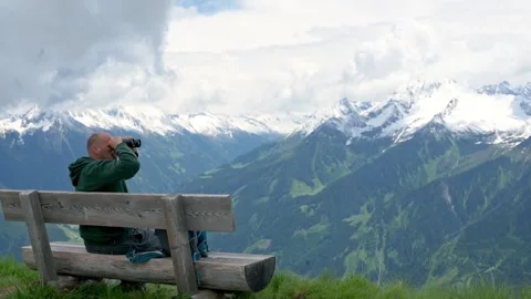 A man sits on a bench using binoculars to observe the stunning snow-covered Stock Footage 283946998