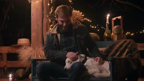 Man sits on a bench on the veranda in the evening and strokes a white dog Stock Footage 166944221