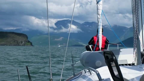 Man sits on bow of ship sailing north sea against mountains Stock Footage 168370596