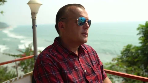 A man sits in a cafe at a table by the sea and smokes a cigarette. Stock Footage 74760887