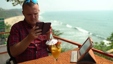 A man sits in a cafe at a table uses a phone Stock Footage 74759420