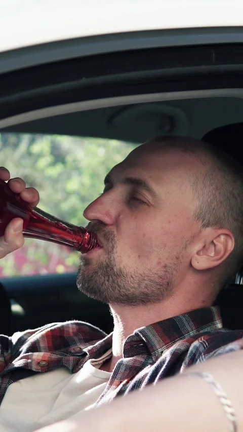 A man sits in a car and drinks alcohol. Drinking while driving, stress. Vidéo 330117917