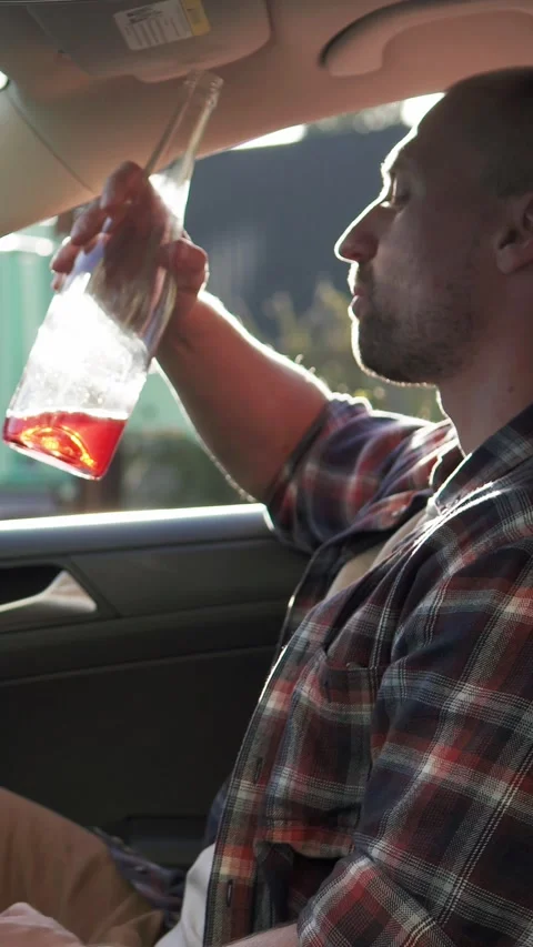 A man sits in a car and drinks alcohol. Drinking while driving, stress. Видео 330117919