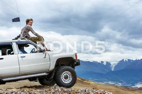 Man sits on the car SUV the mountains wheel Stock Photos