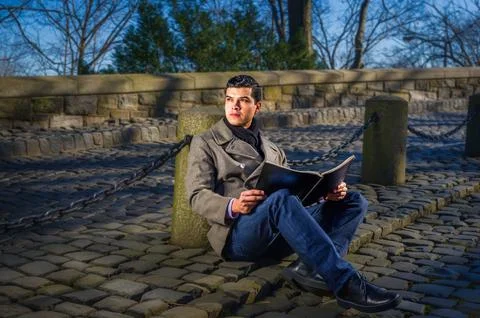 A man sits on a cobblestone path, reading a book Stock Photos