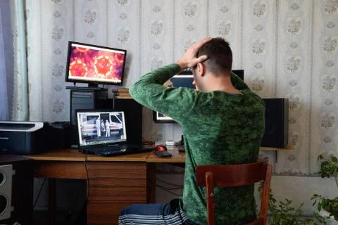 A man sits at computer monitors and is horrified by the news about the spread of Stock Photos