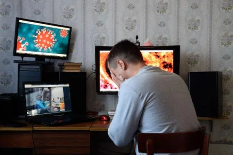 A man sits at computer monitors and is horrified by the news about the spread Stock Photos