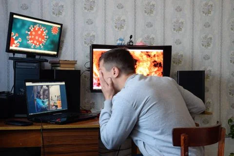 A man sits at computer monitors and is horrified by the news about the spread Stock Photos