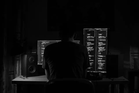 A man sits at a computer in a room at a table at night with blue lighting and Foto stock