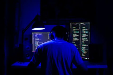 A man sits at a computer in a room at a table at night with blue lighting and Foto stock