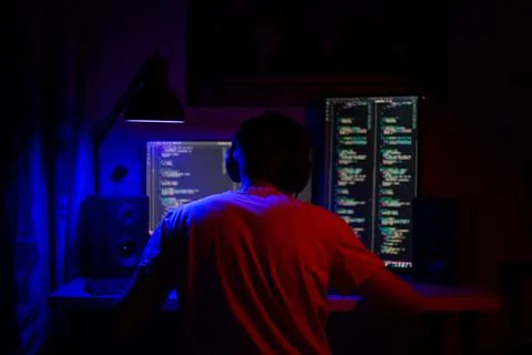 A man sits at a computer in a room at a table at night with blue lighting and 库存照片