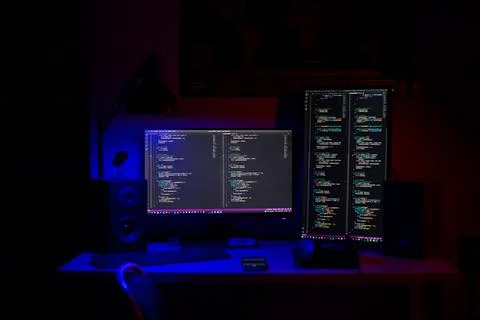 A man sits at a computer in a room at a table at night with blue lighting and Stock-Fotos