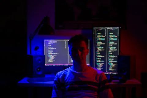 A man sits at a computer in a room at a table at night with blue lighting and 库存照片