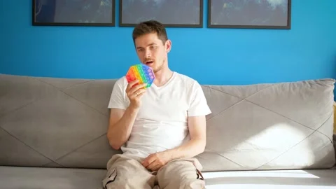 A man sits on the couch and looks comically at pop it. Tired of trends Stock Footage 155724786