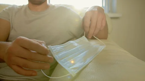 Man sits on a couch and puts on a medical mask Stock Footage 129824998