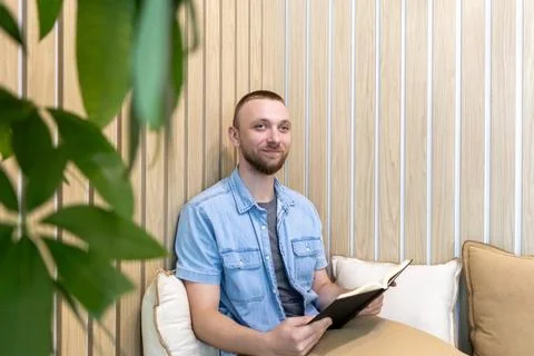 A man sits on a couch with cushions while reading a book.  写真素材