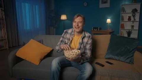 A man sits on the couch in the evening, eats popcorn and watches TV. A man Foto stock