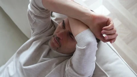 A man sits on the couch with his hands folded on his forehead, looks ahead Stock Footage 152656442