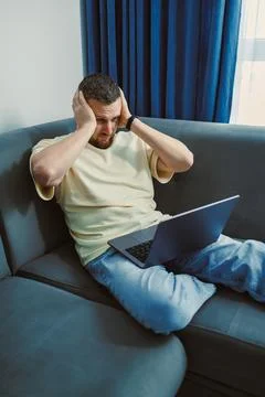 A man sits on a couch with his hands on his head showing signs of frustration Stock Photos