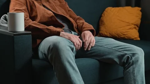 A man sits on a couch, holding a coffee mug with both hands. He makes subtle Video stock 339097574