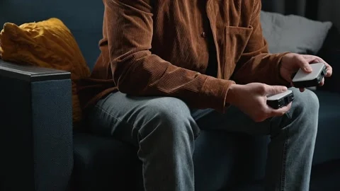 A man sits on a couch, holding a mobile device in his hands while focused on the Video stock 339097709