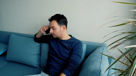 A man sits on the couch at home and angry talks on the phone, drops the phone Stock Footage 169302891