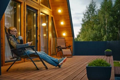 Man sits with a cup of tea in the evening on the terrace illuminated by out.. Stock Photos