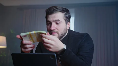 A man sits at a desk holding a stack of dollar bills and two golden coins, .. Stock Footage 296269598