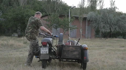 Man sits down on old motorcycle and leaves from green lawn Stock Footage 85691909