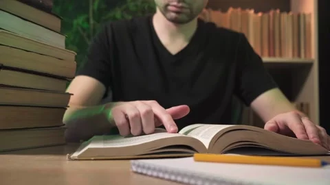 A man sits down at a table, opens a book and starts reading Stock Footage 264130983