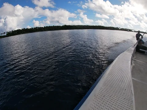 Man sits on the edge of a boat that is speeding across a lagoon Video stock 121806323