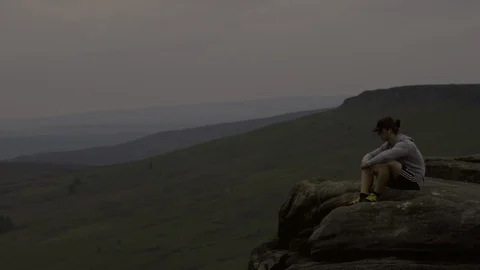 Man sits on the edge of a cliff after a run  Stock Footage 85657191