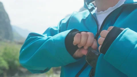 A man sits on the edge of a cliff in a blue anorak and takes out his glasses Stock Footage 166065669