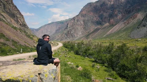 A man sits on the edge of a cliff wearing a black anorak. Katu-Yaryk canyon Video stock 165967167