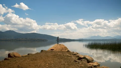 A man sits at the edge of an old pier on a mountain lake and enjoys the view Stock Footage 89213374