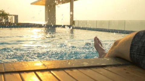 The man sits on the edge of the pool and wets his feet in the water. a luxurious Stock-Footage 87189009