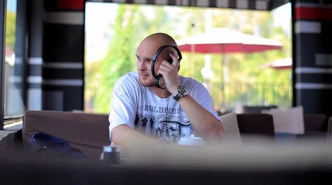 A Man Sits in the Empty Cafe Listening to Music With Headphones and Looking Out Stock Footage 66690096