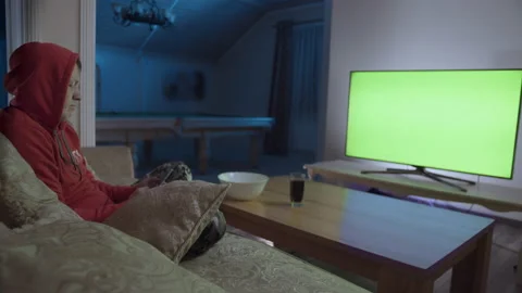 A man sits in the evening on a couch with a mobile phone in front of a green Stock Footage 155397030