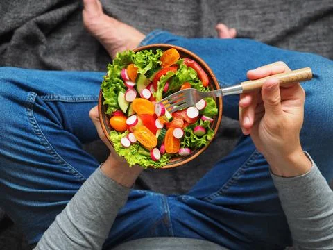 A man sits on the floor and eats a delicious green salad 스톡 사진