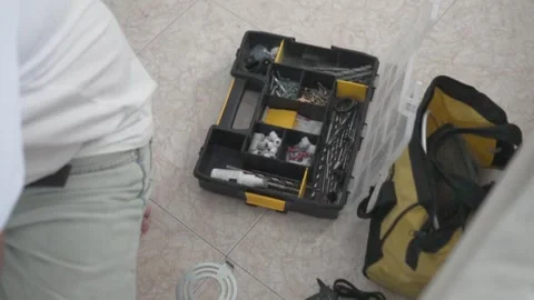 A man sits on the floor next to a toolbox filled with drills, screws, and repair Stock Footage 316294253