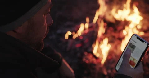 Man sits by the forest fire with smartphone in his hands. Video stock 131539979