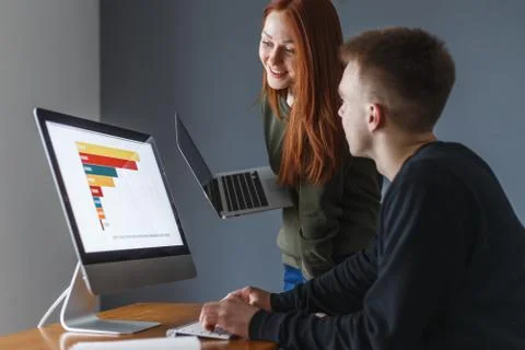 A man sits in front of the computer and tells the woman something. Shows the  Stock Photos