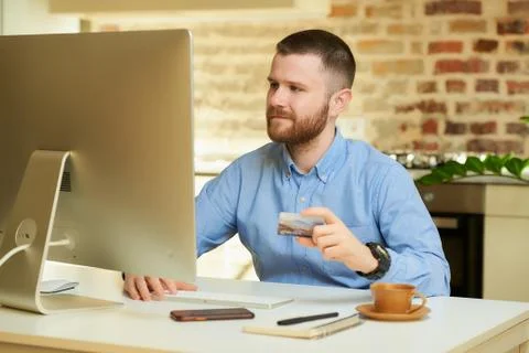 Man sits in front of the computer and holding a credit card at his hand at ho Stock Photos