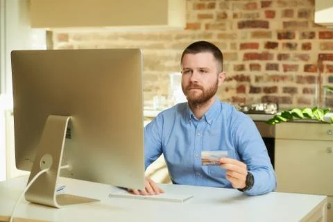 Man sits in front of the computer and types card information on an online sto Stock Photos
