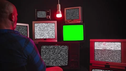 A man sits in front of group of 9 vintage TV with chroma key screens in room Stock Footage 169864471
